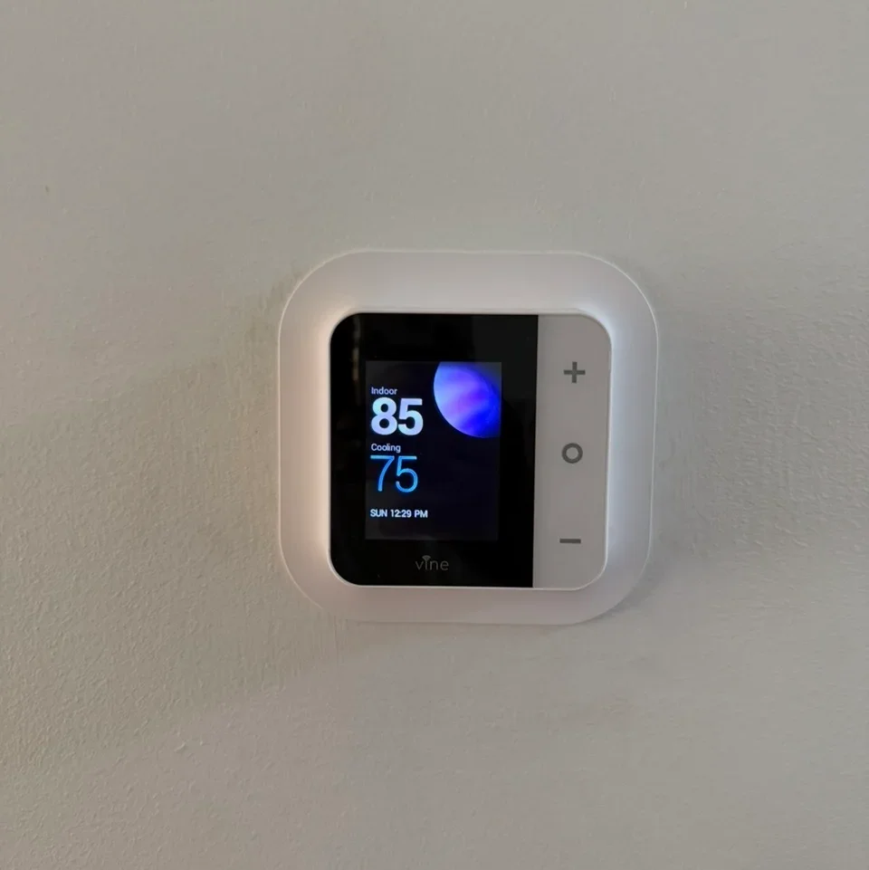White smart thermostat with touchscreen display mounted on drywall, showing temperature and cooling settings